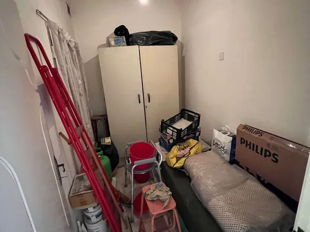 a room with a bed, a refrigerator, and a trash can