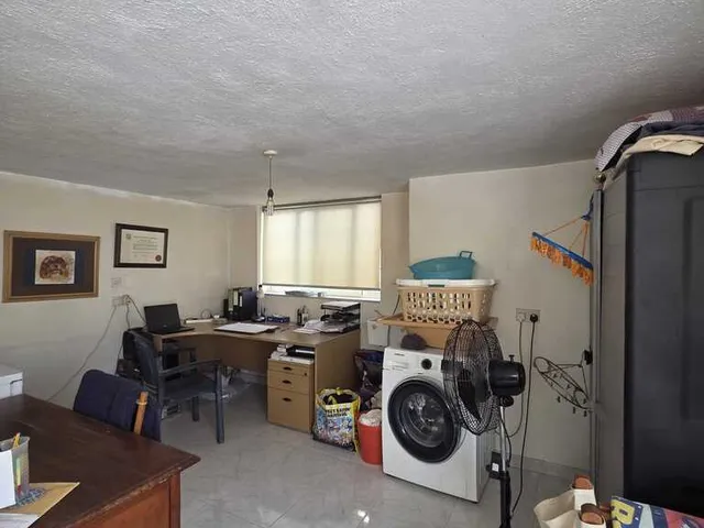 a room with a desk, a refrigerator, a window and a bed